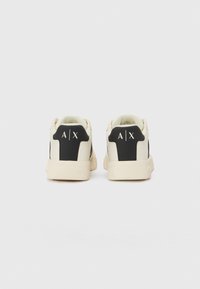 Hvite sneakers med en teksturert svart hæl og logo, med en glatt overdel og en litt klumpete såle. Minimalistisk design totalt sett.