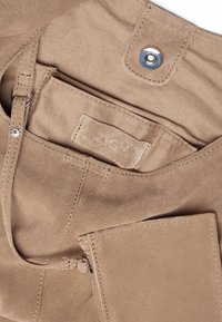 Torebka zamszowa w odcieniu brązowym z zamykaną kieszenią, zapięciem na zatrzask i etykietą z materiału. Tekstura jest miękka, z widocznymi detalami przeszycia.