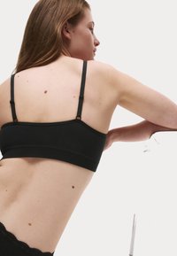 Bralette negro con finas tirantes ajustables, textura acanalada y diseño sin costuras. Estilo minimalista sin hardware visible ni adornos.
