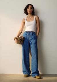 Ľahký biely rebrovaný tielko, voľné širšie modré denimové nohavice so sťahovacou šnúrkou a olivovo zelená kabelka. Obuv má jedinečný dizajn s rozdelenými prstami.