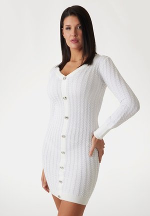 Robe longue à manches longues en maille côtelée blanche avec encolure en V et fermeture à boutons argentés sur le devant. Présente une silhouette ajustée et des poignets contrastés.