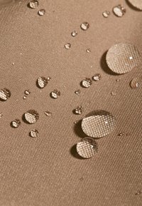 Tessuto impermeabile di colore marrone chiaro con diverse dimensioni di gocce d'acqua che riflettono una superficie testurizzata. Finitura liscia e opaca con accenti lucidi.
