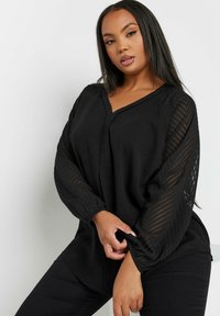 Black blouse with a V-neck, long sheer striped sleeves, and elastic cuffs. Made from lightweight fabric with a relaxed fit.