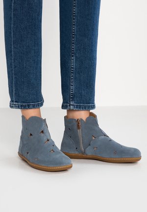 Blå ruskind ankelsstøvler med udskårne mønstre og sidelommer, båret med blå denim jeans.