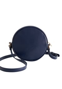 Sac bandoulière rond en cuir bleu marine avec une texture lisse, des accents en métal doré, et une sangle ajustable, arborant un logo embossé sur le devant.