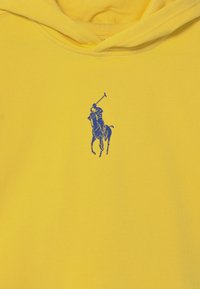 Gelbe Kapuzenjacke aus weichem Baumwollstoff mit einem blauen Polo-Spieler-Emblem auf der Brust. Glatte Textur und Detail mit Kordelzug an der Kapuze.