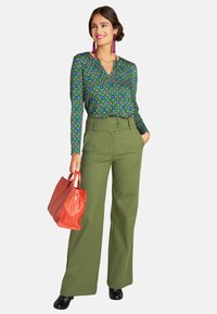 Long-sleeve green blouse with floral pattern, high-waisted olive green pants, and a red leather handbag. Black shoes complete the outfit.
