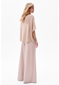 Licht beige gebreide top met een gelaagd patroon, gecombineerd met wijde pastelroze broek. Zachte textuur met een losvallende pasvorm.