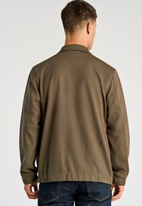 Kurtka oliwkowozielona z kołnierzem, ściągaczami na rękawach i lekko teksturowanym wykończeniem. Charakteryzuje się luźnym krojem i widocznymi przeszyciami wzdłuż szwów.