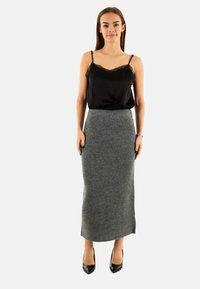 Camisola in satin nero con inserti in pizzo, abbinata a una gonna a tubino grigia in lana, lunga fino al ginocchio. La modella indossa tacchi alti neri. Design semplice ed elegante.