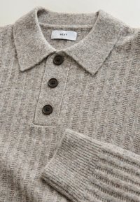Graues geripptes Strick-Poloshirt mit Kragen, drei braunen Knöpfen und einem Etikett mit der Aufschrift "NEXT". Weiche Textur und lässiges Design.