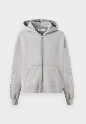 Sudadera con capucha gris y cremallera completa, con detalles de tachuelas en las mangas y bolsillos tipo canguro. Material de algodón suave.