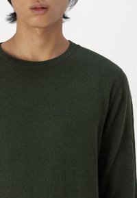 Mørkegrønn strikket genser med rund hals og lange ermer. Stoffet ser mykt ut med en subtil tekstur.