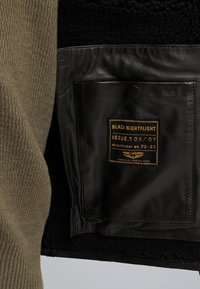 Groene ribbelstof buitenkant, zwarte lederen binnenkant met een zak. Label leest "BLACK NIGHTFLIGHT ISSUE.508/07 PME LEGEND."
