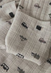 Bomullstyg i beige med en texturerad, vävd mönstring som har små illustrationer av svarta och grå fordon samt resväskor.