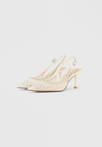 Beige slingback-hæle med spidse tæer, pyntet med klare og iriserende ædelsten, tynde ankelstropper og slanke hæle.