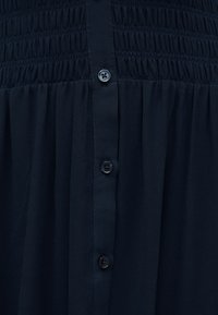 Φόρεμα σε ναυτικό μπλε με σμιγωμένο μπούστο, απαλό ρέον ύφασμα και σειρά από τέσσερα μαύρα κουμπιά στο μπροστινό μέρος για κλείσιμο.