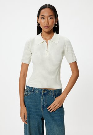 Geribbelde, créme kleurige polo met korte mouwen, voorzien van een kraag en knoopsluiting, gecombineerd met ontspannende blauwe denim jeans.