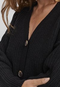 Zwart gebreide cardigan met V-hals, lange mouwen en twee grote knopen. De textuur is chunky en de pasvorm lijkt ontspannen.