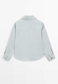 Camicia azzurro chiaro a maniche lunghe con collo, orlo curvo e polsini con bottoni. Tessuto liscio con una texture sottile e dettagli a contrasto in nero.