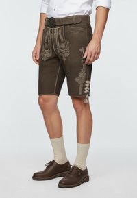 Braune Lederhosen mit aufwendigen Stickdetails, knielanges Design, kombiniert mit beigen Kniestrümpfen und braunen Schnürschuhen.