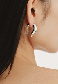 Pendientes plateados y transparentes con un diseño curvado y asimétrico. Acabado metálico suave complementado por elementos transparentes.