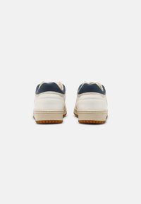 Sneaker bianche e blu navy con finitura in pelle liscia, imbottitura texturizzata e suola in gomma. Cuciture visibili e occhielli per i lacci.