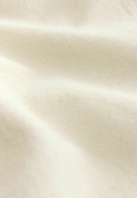 Tessuto di cotone color crema, che presenta una trama liscia con lievi pieghe e un motivo di tessitura fine, evidenziando la sua morbidezza e durabilità.