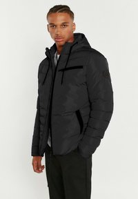 Doudoune noire avec capuche, dotée de poches zippées, d'une surface texturée et d'un patch logo sur la manche gauche.