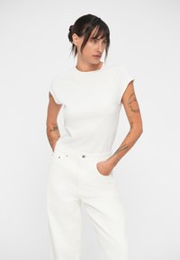 Haut blanc à manches courtes associé à un pantalon blanc taille haute. Le haut a un col rond et une silhouette ajustée, fabriqué à partir d'un tissu lisse.