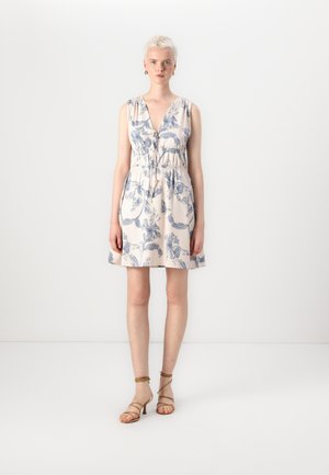 Robe à motifs floraux en beige clair avec des dessins bleus, décolleté en V profond, taille élastique et jupe évasée. Portée avec des talons beiges à lanières.