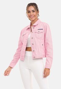 Roze denimjack met een klassieke kraag, voorzakken, zilveren hardware en verwerkte details. Draag het open over een witte top.
