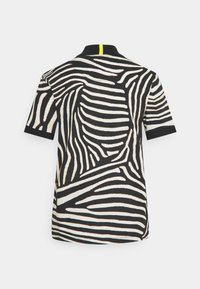 Koszulka polo z krótkim rękawem w czarno-białym wzorze zebry, z czarnym kołnierzykiem i żółtym akcentem na plecach przy dekolcie.