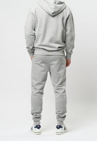 Grauer Sweatshirt- und Jogginganzug aus weichem Stoff. Mit Kapuze, gerippten Bündchen und seitlichen Taschen. Die Schuhe sind weiß mit marineblauen Akzenten.