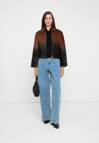 Braune und schwarze Ombre-beschnittene Jacke, schwarzes Oberteil, hellblaue weit geschnittene Jeans und schwarze Handtasche, mit glattem Ledertextur und kastenförmiger Silhouette.