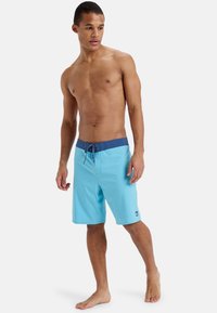 Un maillot de bain bleu clair avec une taille azul foncé, doté d'une fermeture à cordon. Fabriqué à partir d'un tissu lisse et à séchage rapide.