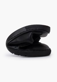 Zapatos negros sin cordones con una suela de goma texturizada, parte superior de cuero suave y puntera redondeada, que cuentan con un diseño plegado para un almacenamiento compacto.