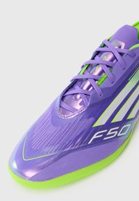 Lilla og grøn indendørssko til sport med snørebånd, "F50" branding og tekstureret overdel på en hvid baggrund.