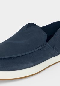 Chaussure décontractée bleu marine sans lacets avec dessus en daim, semelle intermédiaire blanche et semelle extérieure en caoutchouc marron clair, avec des détails de couture minimaux.