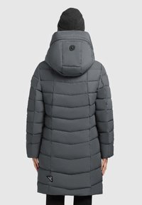 Căciulă călduroasă gri cu capotă, având o textură matlasată, cusături orizontale și un accent cu logo aproape de margine. Căciulă neagră pe cap.