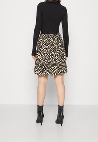 Svart långärmad topp i kombination med en svart och krämfärgad prickig utställd kjol med volangkant. Svarta högklackade ankelstövlar fulländar looken.