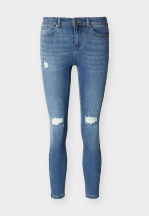 Ozke kavbojke iz svetlo moderega denima, z raztrganimi predeli na kolenih, z zasnovo s petimi žepi in klasičnim pasom z zaponko na gumb.