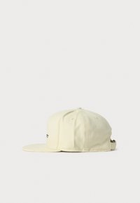 Gorra de béisbol color crema con visera plana y correa ajustable, mostrada desde el lado derecho sobre un fondo blanco liso.