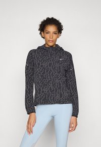 Black patterned lightweight jacket with a hood, featuring a full zipper and reflective accents, paired with light blue leggings.