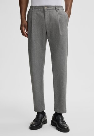 Gray patterned trousers with a tailored fit, featuring a single button closure, pleats, and side pockets, paired with black loafers.