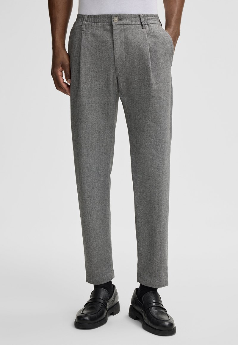 Gray patterned trousers with a tailored fit, featuring a single button closure, pleats, and side pockets, paired with black loafers.