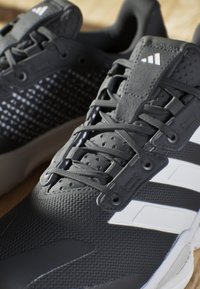 Gray athletic shoes with a textured mesh upper, featuring black accents, white three-stripe logo, and rubber sole. Laces are gray.