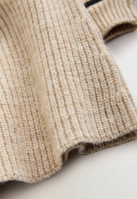 Beige strikket stof med en ribbet tekstur, blød og let fuzzy finish, draperet for at vise kurver og dybde.