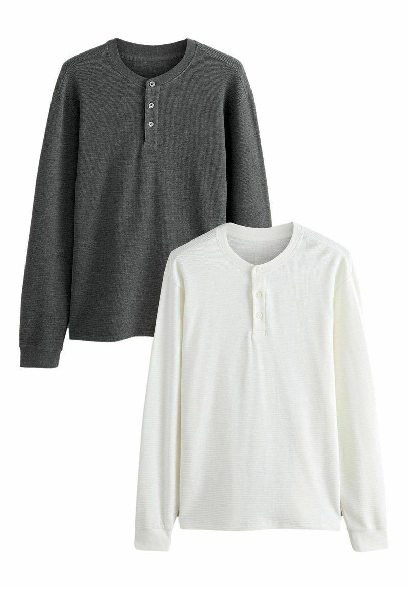 Due camicie henley a maniche lunghe: una in tessuto a coste grigio scuro con tre bottoni, l'altra in tessuto a coste bianco con tre bottoni.