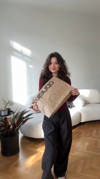 Brun papirindkøbspose med "opuntia" i fed sort tekst. Indstillingen har lyse trægulve, en hvid sofa og indendørs planter.